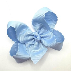 May include: A light blue hair bow constructed from ribbed grosgrain ribbon. The bow features a multi-layered design with scalloped edges along the perimeter of each loop, creating a voluminous and textured appearance against a plain white background.