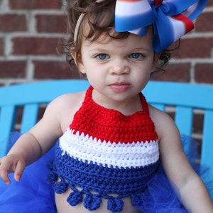 May include: A red, white, and blue crochet halter top and a blue tulle skirt. A large red, white, and blue bow is in the child's hair. The outfit is patriotic and suitable for a holiday.