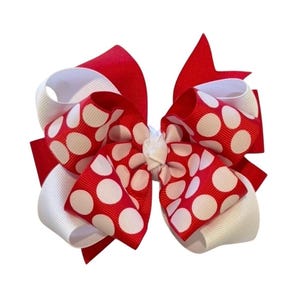 May include: A large, layered hair bow featuring red, white, and red polka dot ribbons. The bow is a vibrant accessory, with a classic design. The bow is suitable for various occasions and adds a pop of color.