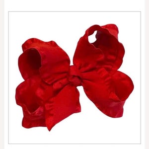 May include: A bright red hair bow constructed from a wide, ruffled fabric ribbon. The accessory features a central knot that gathers the material into two large, voluminous loops on each side, creating a layered and textured appearance throughout.