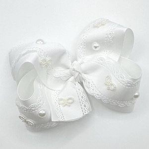 May include: A large, white hair bow with a layered design. The bow features delicate lace trim and is adorned with small, faux pearls and decorative embellishments. The bow is made of a satin-like ribbon.