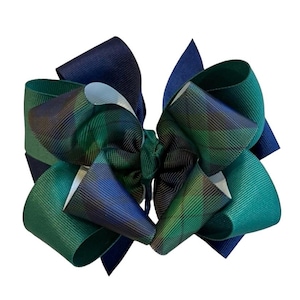 May include: A large, layered hair bow in shades of green, blue, and navy. The bow features a plaid pattern and is made of a grosgrain ribbon. The bow is a decorative accessory.