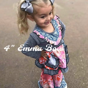 May include: Two grey hair bows, each 4 inches in size, worn in pigtails. The bows are made of a smooth, solid grey fabric and feature a classic, multi-looped design. These hair accessories are styled to sit prominently on top of the head.