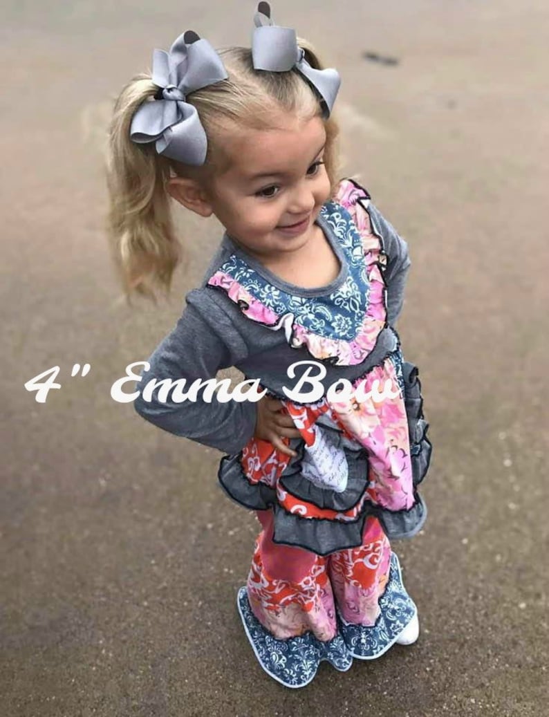 May include: Two grey hair bows, each 4 inches in size, worn in pigtails. The bows are made of a smooth, solid grey fabric and feature a classic, multi-looped design. These hair accessories are styled to sit prominently on top of the head.