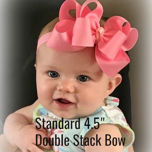 May include: A baby girl wearing a pink and white patterned dress with a large pink double stack bow headband. The headband is 4.5 inches wide. The text "Standard 4.5" Double Stack Bow" is visible in the image.