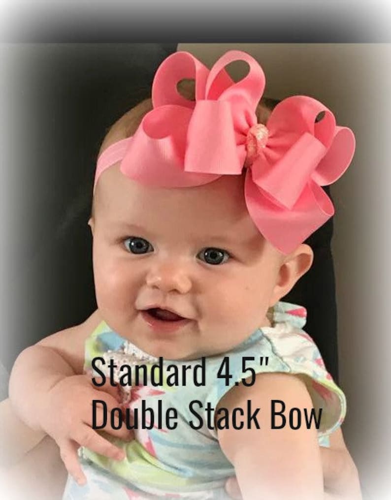 May include: A baby girl wearing a pink and white patterned dress with a large pink double stack bow headband. The headband is 4.5 inches wide. The text "Standard 4.5" Double Stack Bow" is visible in the image.
