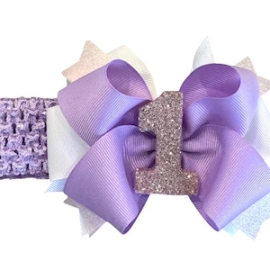 May include: Purple and white headband with a large purple bow and a sparkly pink number one.