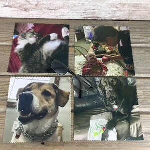 May include: Four square microfiber cloths with different images printed on them. The top left cloth features a cat, the top right cloth features a boy looking at a baby, the bottom left cloth features a dog, and the bottom right cloth features a black dog.