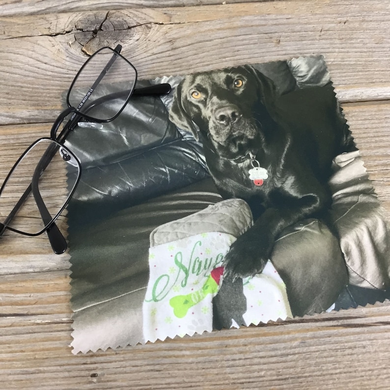 May include: A black Labrador Retriever dog sitting on a couch with a Christmas stocking that says "Have a Holly Jolly Christmas". The dog is wearing a collar with a tag.
