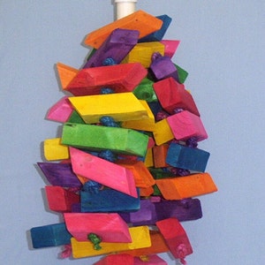 May include: A colorful wooden toy for birds, made of various colored blocks, hanging from a white rope. The toy is shaped like a pyramid and is designed to be interactive for birds.