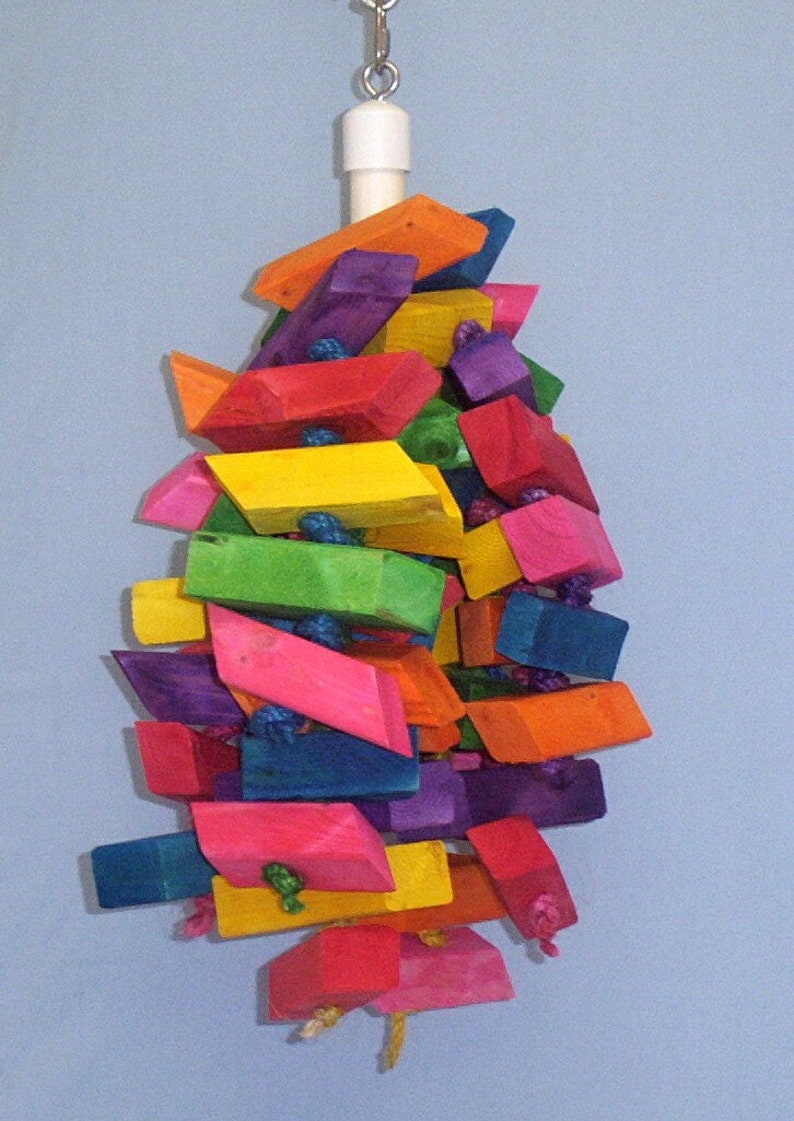 May include: A colorful wooden toy for birds, made of various colored blocks, hanging from a white rope. The toy is shaped like a pyramid and is designed to be interactive for birds.