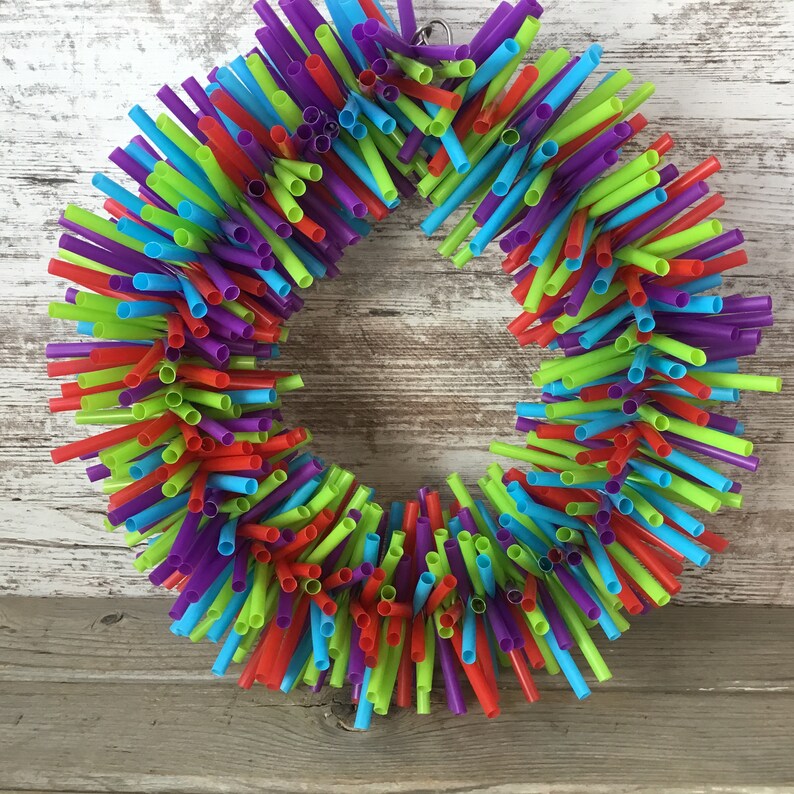 Pu&ograve; includere: Una ghirlanda colorata realizzata con cannucce di plastica per bere in tonalit&agrave; di rosso, verde, blu e viola. La ghirlanda &egrave; circolare e ha un aspetto rustico e fatto a mano.