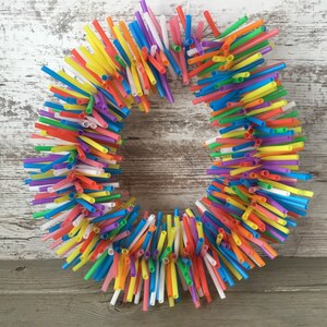 Pu&ograve; includere: Una ghirlanda colorata realizzata con cannucce da bere. Le cannucce sono disposte in cerchio e sono di vari colori, tra cui rosso, arancione, giallo, verde, blu, viola e rosa.