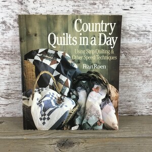 May include: A book titled "Country Quilts in a Day" with text about strip quilting techniques. The cover features a rustic wooden background and a basket filled with colorful quilts. The book is by Fran Roen.