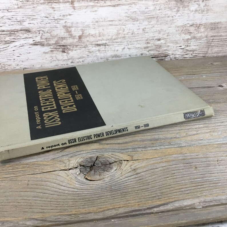 以下が含まれることがあります： 「USSR Electric Power Developments 1958-1959」というタイトルのヴィンテージ本。本は、黒いテキストと黒い長方形のセクションが付いた、明るい灰色の表紙です。「A report on」とタイトルが含まれています。本は木製の表面にあります。