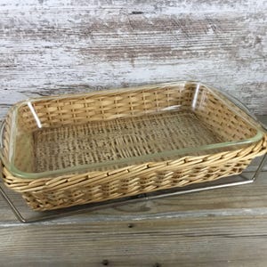 May include: Rectangular baking dish with a clear glass insert and a woven wicker basket. The basket is light brown and sits on a silver metal stand. The dish is designed for baking and serving.