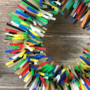 Pu&ograve; includere: Una ghirlanda fatta di cannucce per bere in plastica colorate. Le cannucce sono disposte in cerchio e sono di vari colori, tra cui rosso, blu, verde, giallo e nero.