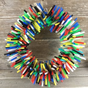 Pu&ograve; includere: Una ghirlanda colorata realizzata con cannucce da bere in rosso, giallo, blu, verde, nero e bianco. Le cannucce sono disposte in forma circolare e legate insieme con un anello di metallo.