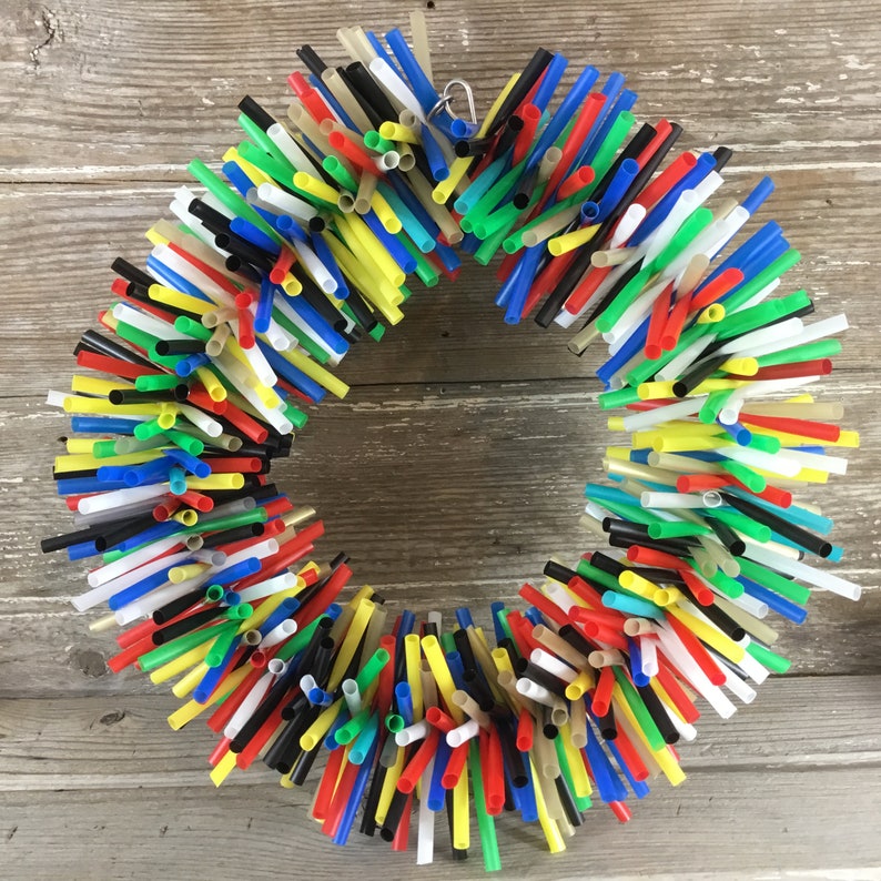 Pu&ograve; includere: Una ghirlanda colorata realizzata con cannucce da bere in rosso, giallo, blu, verde, nero e bianco. Le cannucce sono disposte in forma circolare e legate insieme con un anello di metallo.