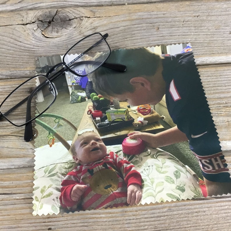 May include: A photo of two siblings, an older brother looking down at his younger brother. The younger brother is wearing a red and white striped shirt with a brown bear design. The older brother is wearing a black and white shirt with the word "SH" on it. The photo is printed on a white fabric with a scalloped edge.