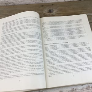 以下が含まれることがあります： 両方のページにテキストが書かれた開いた本。ページはオフホワイトで、テキストは黒です。本は木製の表面に置かれています。テキストは記事またはエッセイのようです。