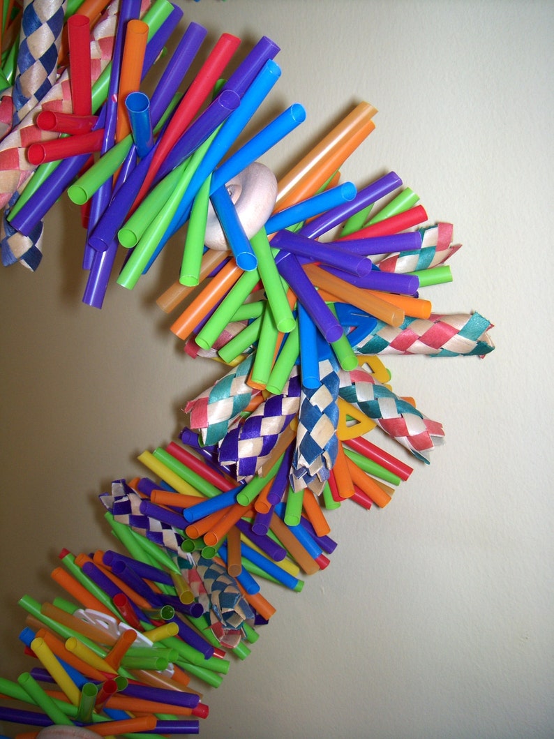 May include: A colorful, woven, hanging toy made from drinking straws and ribbon. The toy is made of various colors, including red, orange, yellow, green, blue, purple, and white. The toy is hanging from the ceiling and is swaying gently in the breeze.