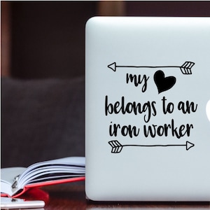 May include: A white laptop with a black vinyl sticker that says "my heart belongs to an iron worker" with arrows on either side of the text.