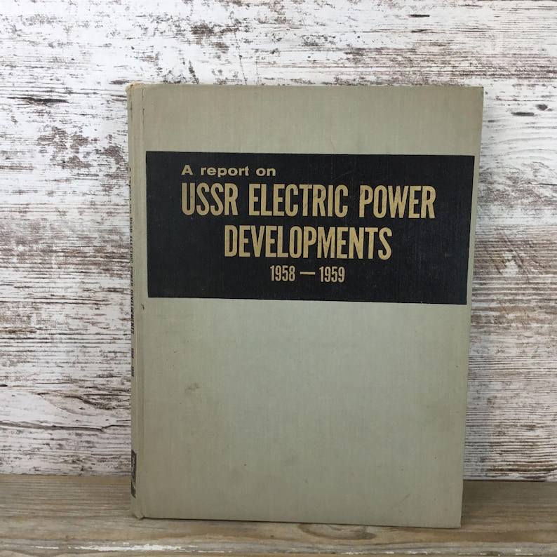 以下が含まれることがあります： 「A report on USSR Electric Power Developments 1958-1959」と題されたヴィンテージ本。本は、黒いテキストが入った明るい灰色の表紙です。テキストは太字のサンセリフ体です。本は木製の表面にあります。