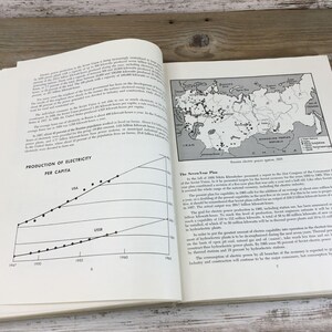 以下が含まれることがあります： テキスト、グラフ、地図が表示された開いた本。左ページには「PRODUCTION OF ELECTRICITY PER CAPITA」というタイトルの折れ線グラフがあります。右ページには、ロシアの地図が表示されています。