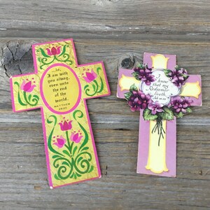May include: Two decorative crosses with religious text. One cross is pink and yellow with floral accents and the text "...I am with you always, even unto the end of the world. Matthew 28:20." The other is purple with flowers and the text "I know that my Redeemer liveth. Job 19:25."
