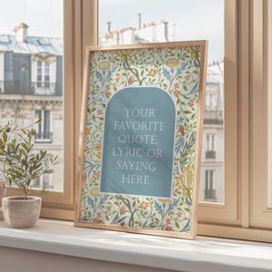 Op de afbeelding: Een ingelijste print met een licht houten frame, met een bloemenpatroonrand in tinten blauw, geel en groen. Het midden heeft een lichtblauwe boog met de tekst: "YOUR FAVORITE QUOTE, LYRIC OR SAYING HERE."