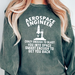 May include: Green sweatshirt with white text that reads "Aerospace Engineer" and a rocket ship graphic. The text below the graphic reads "Crazy enough to blast you into space, smart enough to get you back."