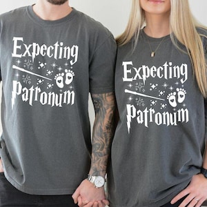 May include: Two gray t-shirts with the text "Expecting Patronum" and a graphic of a wand and baby footprints.