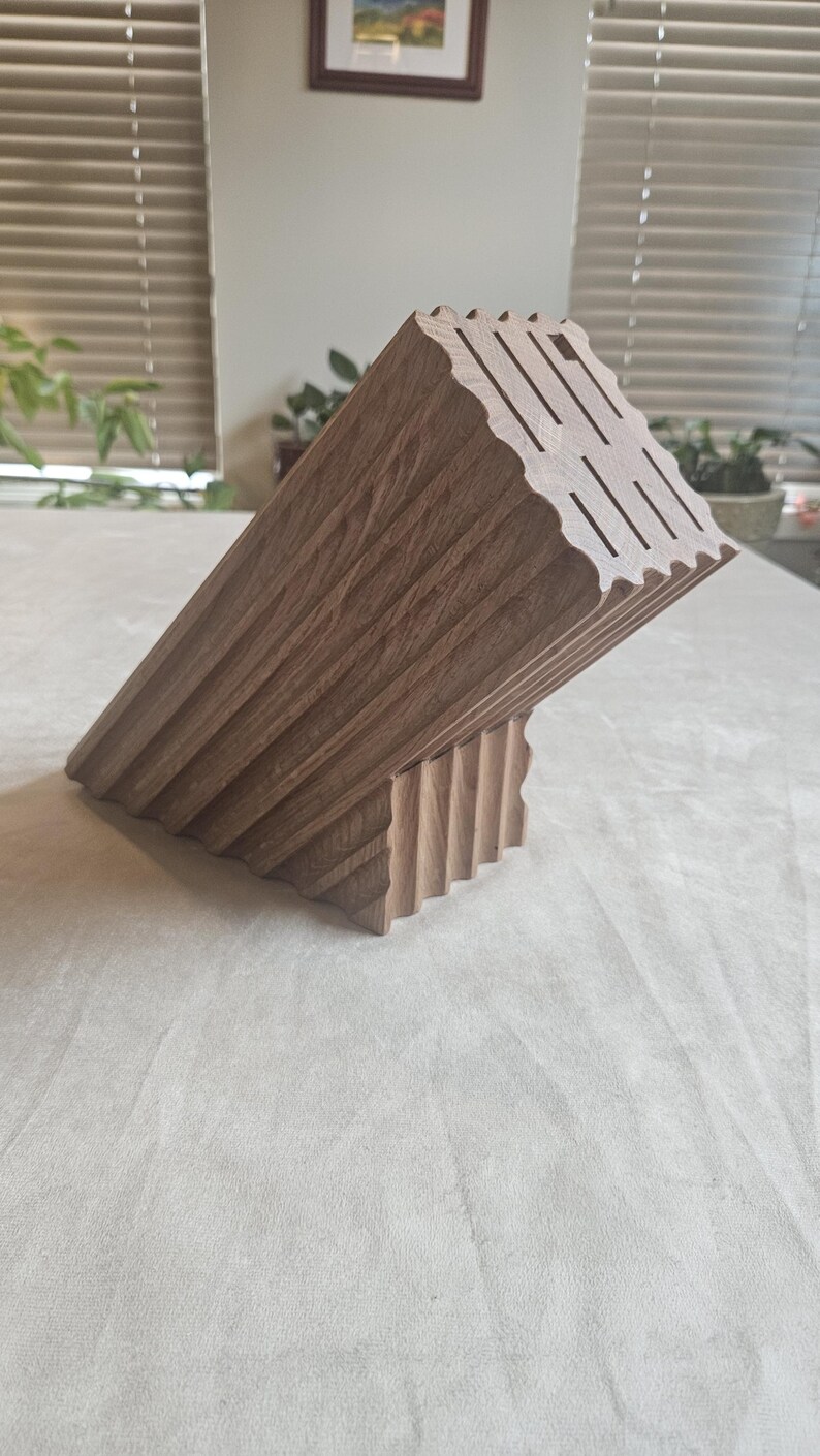 May include: A wooden knife block with a unique, angled design. The block is made of light brown wood and features slots for knives. The design includes a series of vertical grooves and a wavy top edge.