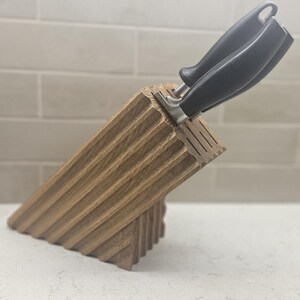 May include: A wooden knife block with a grooved design, holding two knives with black handles. The block is angled, showcasing its textured surface. The kitchen utensil is made of wood.