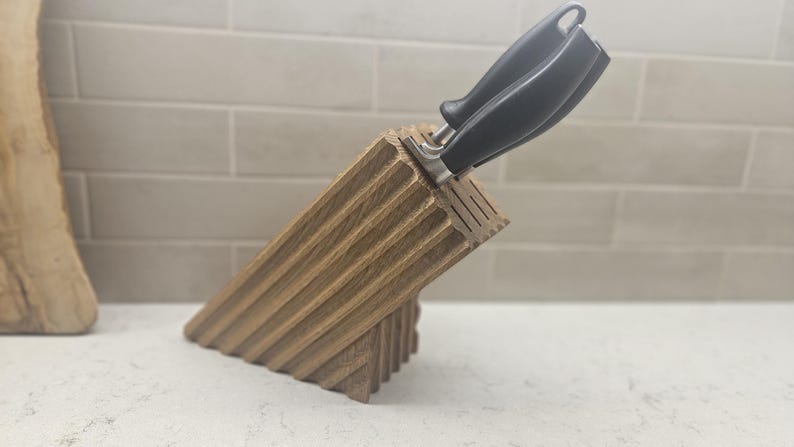 May include: A wooden knife block with a grooved design, holding two knives with black handles. The block is angled, showcasing its textured surface. The kitchen utensil is made of wood.
