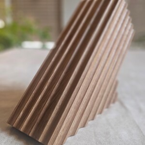 May include: A wooden knife block with a unique, angled design. The block is made of light brown wood and features a series of parallel grooves. The knife block is designed to hold knives and keep them organized.