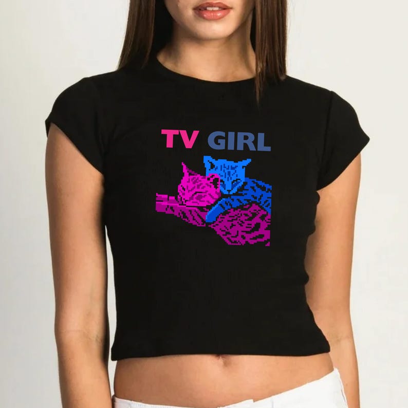May include: Black cropped t-shirt featuring a graphic of two cats cuddling. The text "TV GIRL" is printed in pink and blue lettering on the shirt.