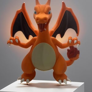 May include: Orange and black plastic toy figure of a dragon with wings, standing on a white platform.