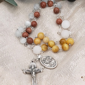 May include: A rosary with multi-colored beads, including white, brown, and yellow, strung on a silver chain. The rosary features a silver crucifix and a medal with religious imagery. The beads are round and smooth.