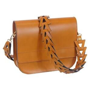May include: A rectangular, tan leather crossbody bag with a unique strap design. The strap features a series of tan leather arrow-shaped cutouts over a black backing. The bag has a flap closure and gold-colored hardware.
