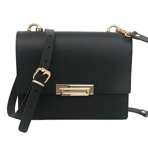 May include: Black rectangular handbag with a gold-colored clasp and buckle. The bag has a long, adjustable strap and a shorter handle. The hardware is gold-toned, and the bag appears to be made of leather or a similar material.