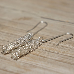 Puede incluir: Un par de pendientes colgantes de plata con un delicado y complejo diseño de malla de alambre. Los pendientes están suspendidos de simples ganchos de plata.