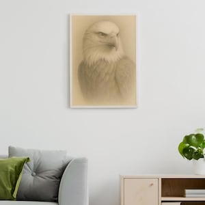 Puede incluir: Impresión enmarcada en tonos sepia de un águila calva. El dibujo a lápiz muestra la cabeza blanca, el pico afilado y la mirada intensa del águila. La obra de arte cuelga de una pared blanca, sobre un sofá gris y un mueble de madera.
