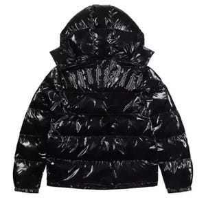 May include: A black puffer jacket with a glossy, reflective finish and a hood. The back features the word TRAPSTAR embroidered in a gothic-style font across the upper section. The jacket has horizontal quilted panels throughout the design.