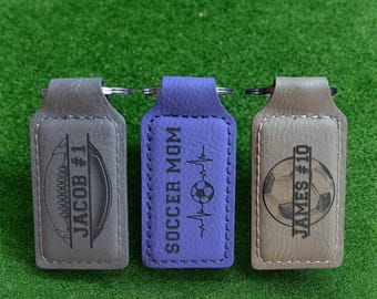 May include: Three leather keychains with different designs. The first keychain is gray with a soccer ball and the text "Jacob #1". The second keychain is purple with a soccer ball and the text "Soccer Mom". The third keychain is gray with a soccer ball and the text "James #10".