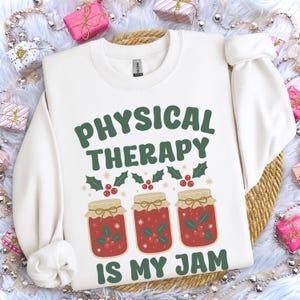 May include: White sweatshirt with the text "PHYSICAL THERAPY IS MY JAM" in green. The design includes three jars of jam with holly and berry accents. The sweatshirt is a crew neck style.