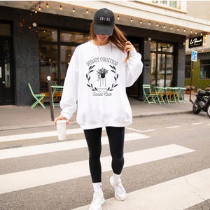 Puede incluir: Sudadera blanca con texto negro que dice "Pothos Collector Social Club" y un gráfico de una planta en maceta con hojas. La sudadera la lleva puesta una persona con una gorra de béisbol negra que dice "11:11".