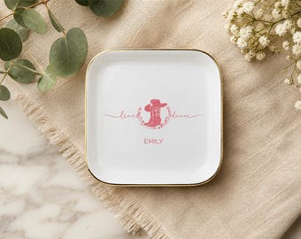 Könnte beinhalten: Eine quadratische weiße Keramikschale mit goldenem Rand. In der Mitte befindet sich eine rosa Grafik eines Cowboystiefels mit Hut, umgeben von einem Blumenkranz, mit dem kursiven Text line dance und dem darunter gedruckten Namen EMILY.