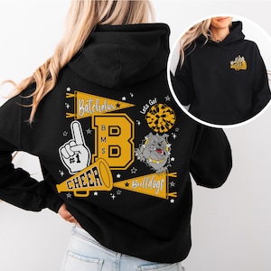 Könnte beinhalten: Schwarzer Kapuzenpullover mit großem gelb-weißem Aufdruck auf dem Rücken. Das Design enthält den Text "Batchelor", "BMS", "CHEER", "Bulldogs", ein Bulldoggen-Maskottchen und einen Cheerleader-Pompon.